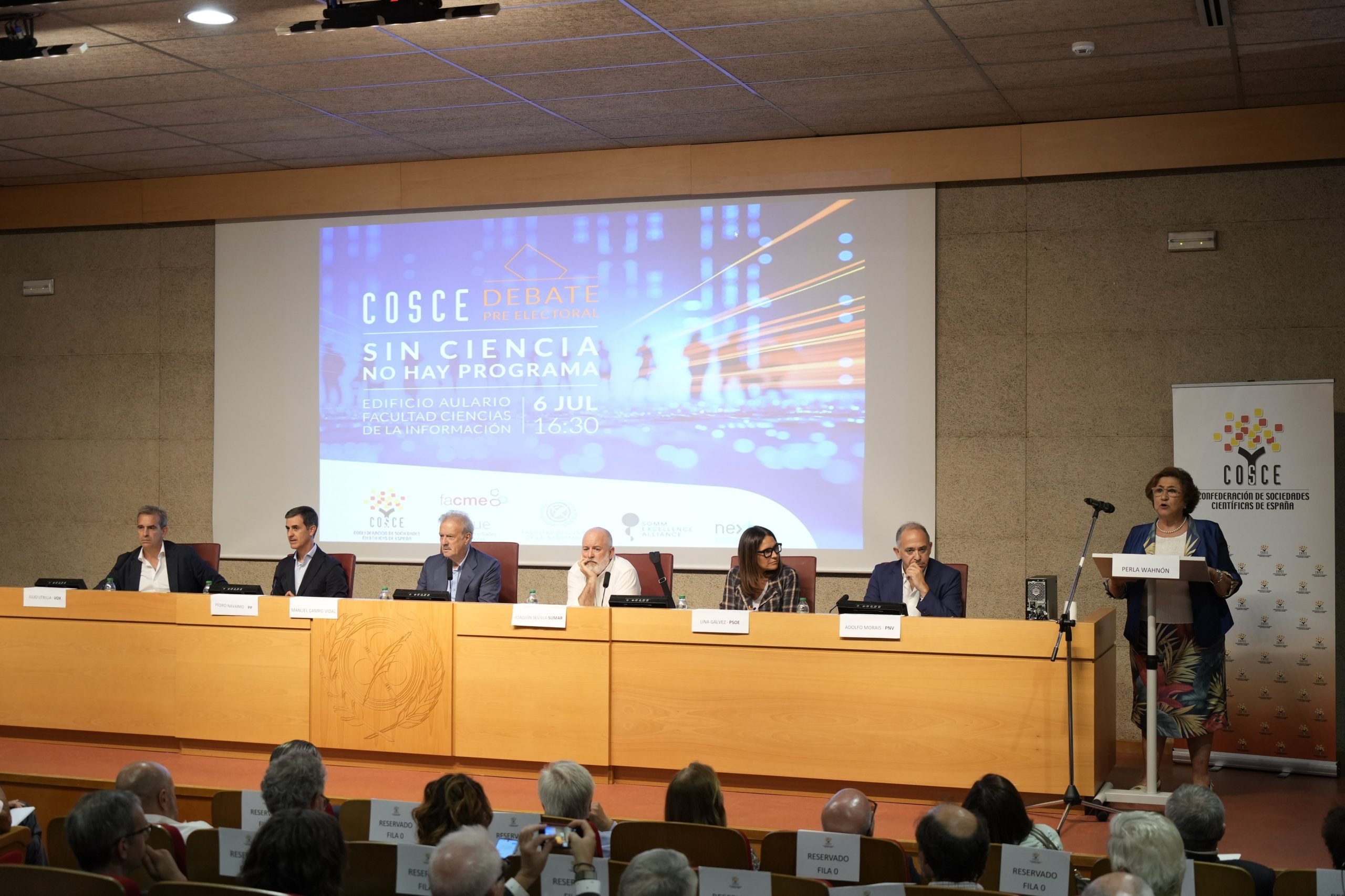 La presidenta de COSCE Perla Wahnón en la inauguración del debate. En la mesa: el periodista Manuel Campo Vidal, Lina Gálvez (PSOE), Pedro Navarro (PP), Julio Utrilla (VOX), Joaquín Sevilla (SUMAR) y Adolfo Morais (PNV) .